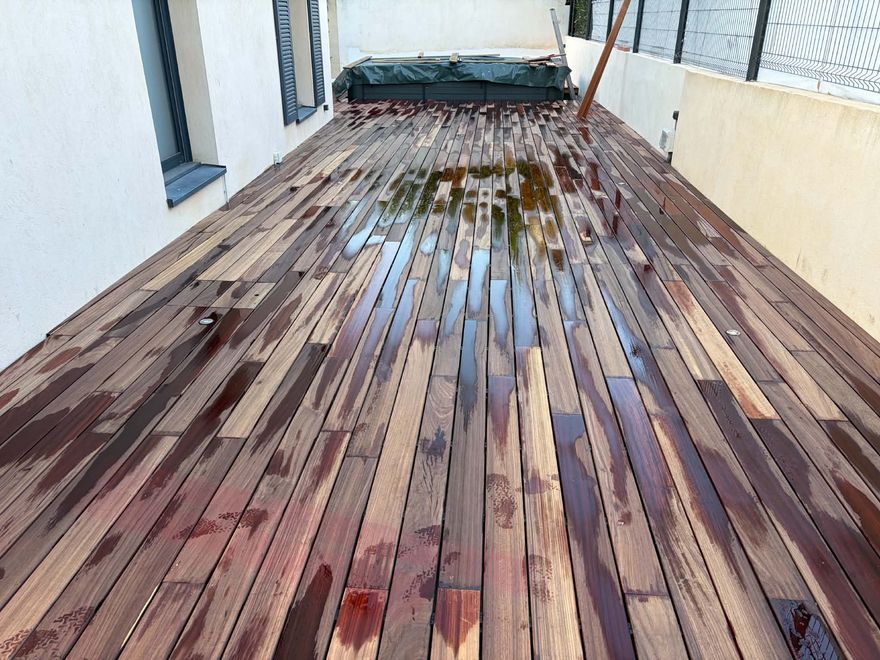 Terrasse en padouk aux teintes rouges et brunes, lames mouillées, juste après la pose